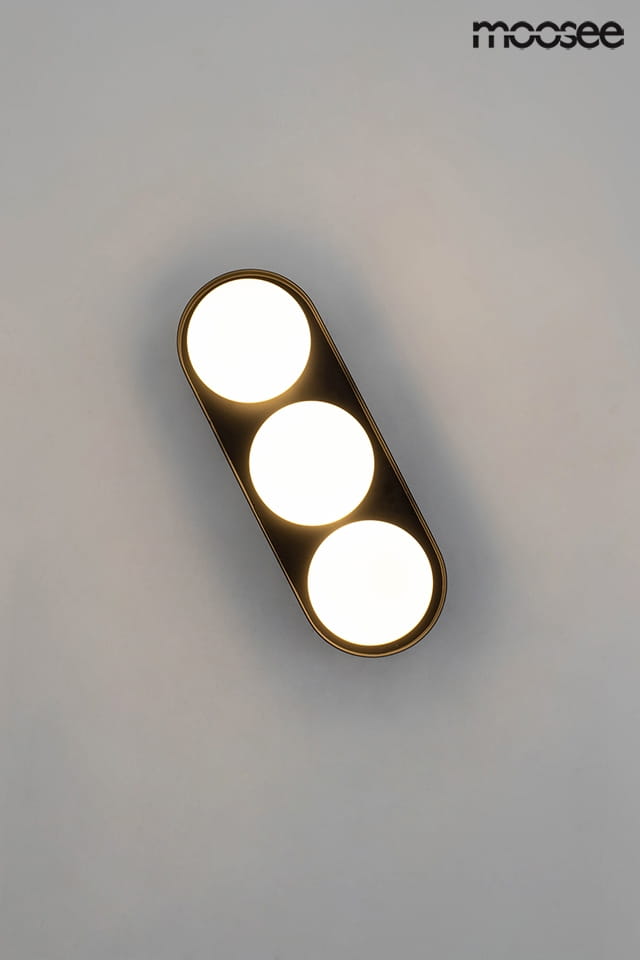 Kinkiet Drops 3-punktowy w kolorze złotym z trzema okrągłymi, białymi kloszami. Ujęcie frontalne, produkt zamontowany na gładkiej, jasnej ścianie. Wymiary i detale nie są widoczne, ale kształt ma elegancki, nowoczesny design.