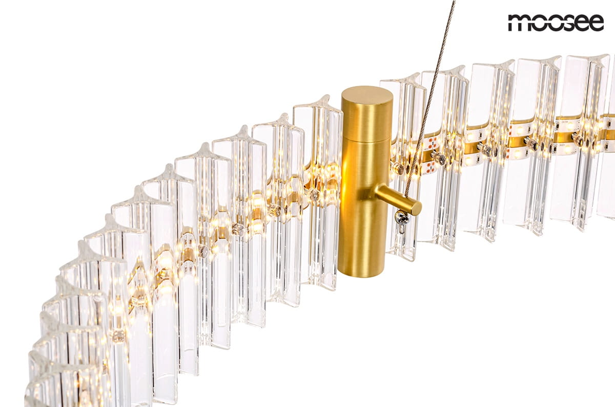 Lampa wisząca Saturnus LED 70, 1-punktowa, w kolorze złotym. Widoczny metalowy uchwyt z przodu oraz przezroczyste klosze w formie prostokątów, które emitują światło. Produkt zawieszony na cienkim przewodzie, z delikatnym, minimalistycznym designem.