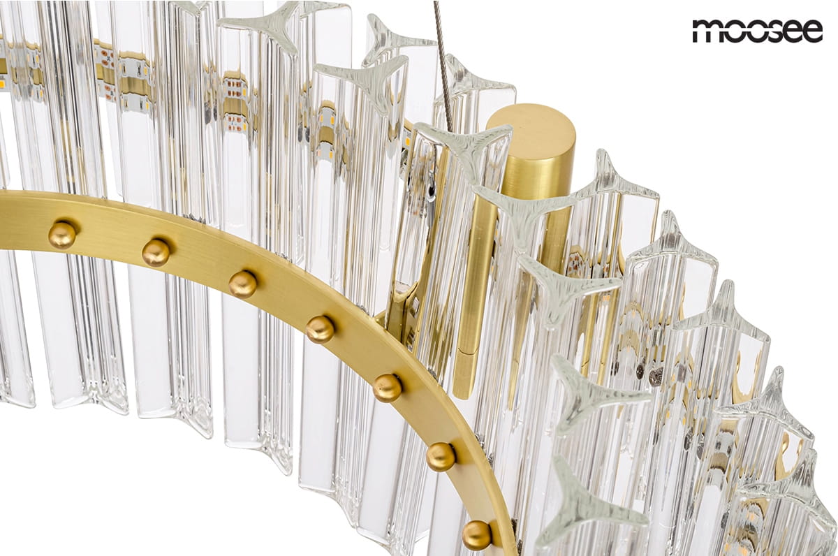 Lampa wisząca Saturnus Due LED 47, 1-punktowa, z okrągłą, złotą oprawą oraz przezroczystymi, teksturowanymi kloszami w kształcie prostokątów. Widoczna metalowa konstrukcja z dekoracyjnymi kulkami. Kąt ujęcia zbliżenie na detal lampy.