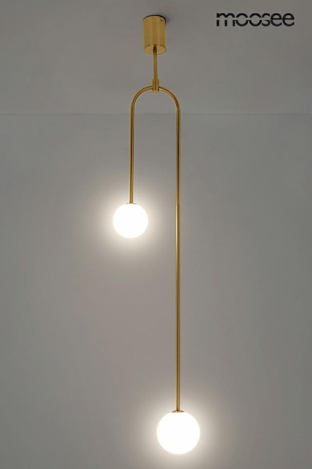 Lampa wisząca 2-punktowa w kolorze złotym, z długim, prostym ramieniem, zawieszona na suficie. Dwie okrągłe, białe żarówki emitujące światło, zawieszone na różnych wysokościach. Tło w jasnym kolorze, minimalistyczne.
