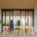 Lampa wisząca Sula 1-punktowa w naturalnym kolorze, o stożkowym kształcie, zawieszona na cienkim przewodzie. Wnętrze w stylu skandynawskim, z drewnianym blatem stołu i roślinami w tle. Jasne tło z dużymi oknami.