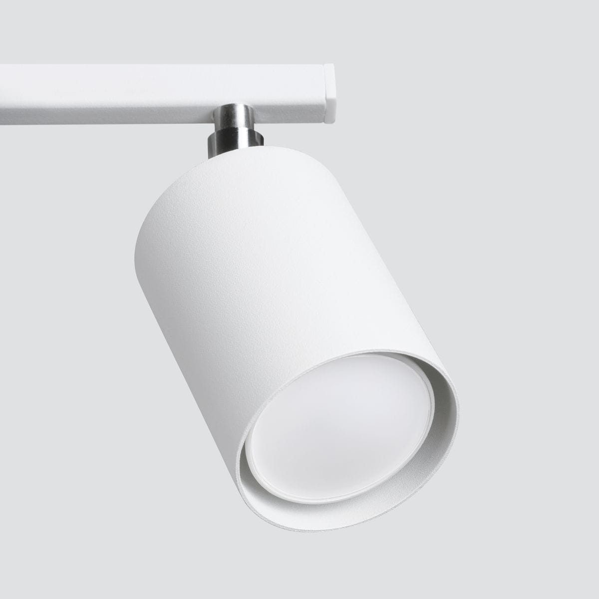 Biała lampa sufitowa Lemmi z trzema punktami świetlnymi, wykonana z matowego materiału. Ujęcie z boku, pokazujące cylindryczny kształt oprawy i jasne, okrągłe źródło światła. Prosta konstrukcja montowana na ścianie.