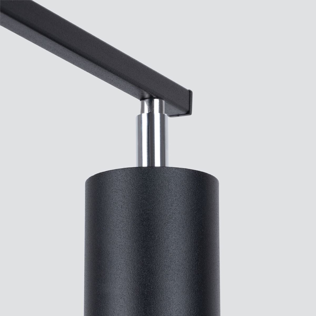 Czarna lampa sufitowa Lemmi, 3-punktowa, z metalowym kloszem o matowej fakturze. Widoczny detal mocowania w postaci metalowego elementu. Ujęcie z boku, skupione na konstrukcji lampy. Tło jasnoszare, minimalistyczne.