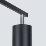 Czarna lampa sufitowa Lemmi, 3-punktowa, z metalowym kloszem o matowej fakturze. Widoczny detal mocowania w postaci metalowego elementu. Ujęcie z boku, skupione na konstrukcji lampy. Tło jasnoszare, minimalistyczne.