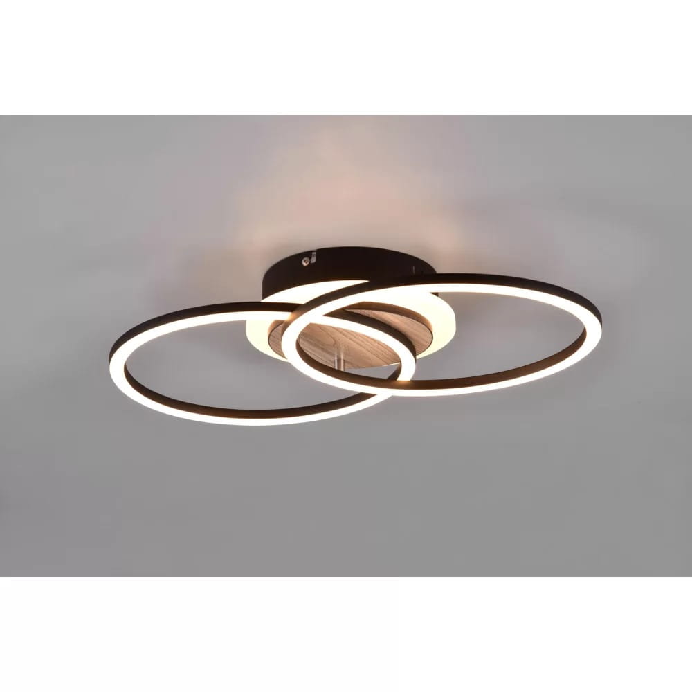 Czarna lampa sufitowa 3-punktowa Giro LED z pilotem, składająca się z dwóch okręgów z podświetleniem LED, z centralnym elementem w kolorze drewna. Ujęcie z dołu, ukazujące nowoczesny design i detale konstrukcji.