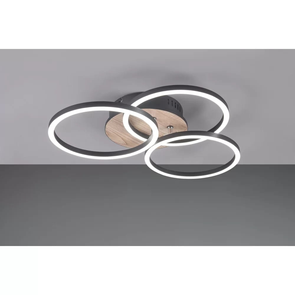 Trzypierścieniowa lampa sufitowa LED w kolorze czarnym z imitacją drewna, z pilotem. Ujęcie z boku, ukazuje okrągłe, podświetlane pierścienie oraz drewniany element montażowy. Idealna do nowoczesnych wnętrz.