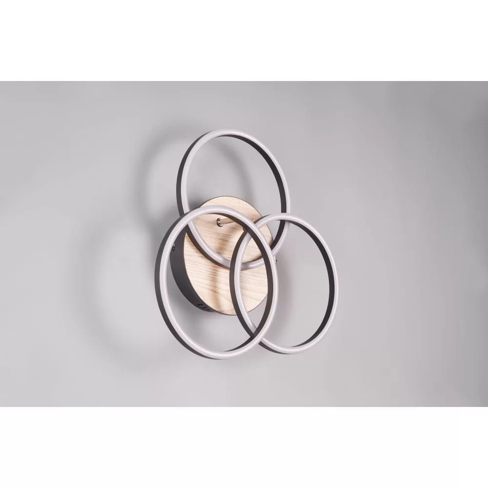 Czarna lampa sufitowa LED 3-punktowa z imitacją drewna, składająca się z trzech okrągłych elementów w różnych rozmiarach. Ujęcie frontalne, lampa zamontowana na ścianie, w tle jasnoszare. Widoczny pilot do zdalnego sterowania.