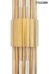 Kinkiet Amadeo 2-punktowy w kolorze złotym. Posiada cylindryczną podstawę z matowego metalu oraz szklane elementy w formie rur, które tworzą efektowną kompozycję. Widok z przodu, na białym tle.