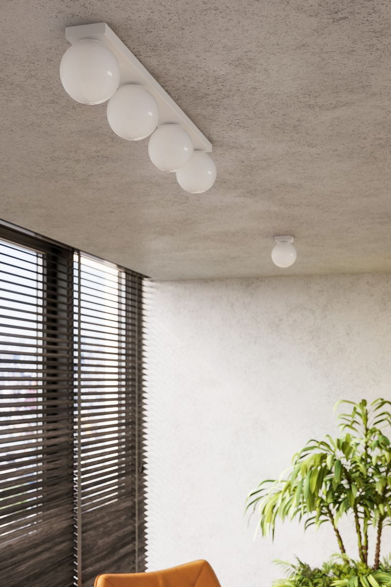 Lampa sufitowa Yoli w kolorze białym, z sześcioma okrągłymi kloszami. Zainstalowana na suficie w aranżacji wnętrza. Klosze mają gładką, błyszczącą powierzchnię. Widoczna tekstura sufitu oraz okna z żaluzjami w tle.