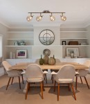 Lentini lampa sufitowa 4-punktowa w kolorze patyny, z czterema przezroczystymi kloszami, zamontowana na górze nad drewnianym stołem. W tle półki z dekoracjami i lustrem, w aranżacji nowoczesnej jadalni.