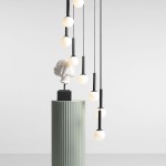 Czarna lampa wisząca Riu z dziewięcioma kulistymi źródłami światła, zawieszona na cienkich przewodach. Produkt umieszczony nad dekoracyjną rzeźbą głowy, na zielonym, żebrowanym postumencie. Tło jasne, minimalistyczne.