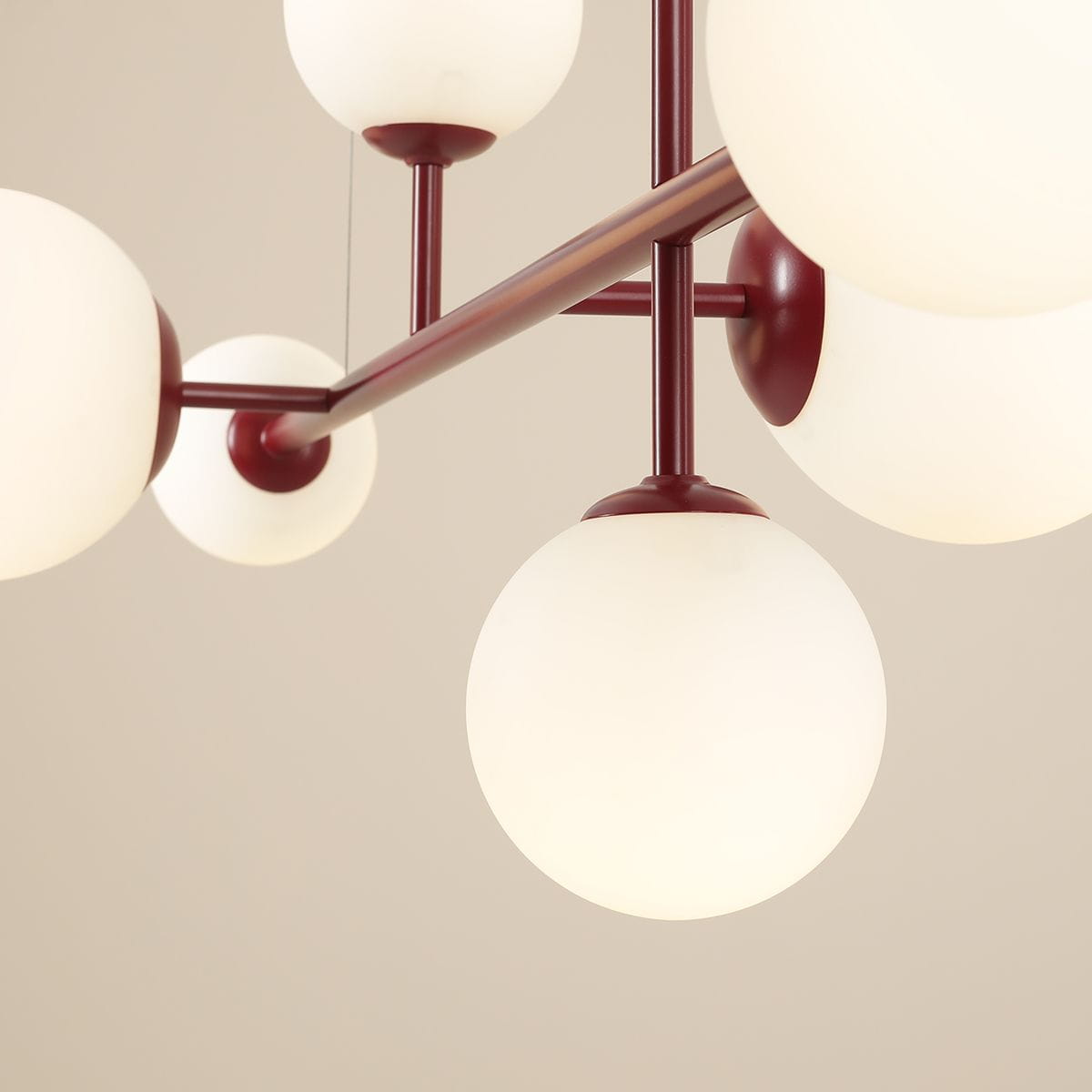 Lampa wisząca Dione w kolorze czerwonym, 6-punktowa, z okrągłymi, matowymi kloszami w białym kolorze. Ujęcie z dołu, prezentujące konstrukcję i detale mocowania. Klosze równomiernie rozmieszczone na metalowym stelażu.