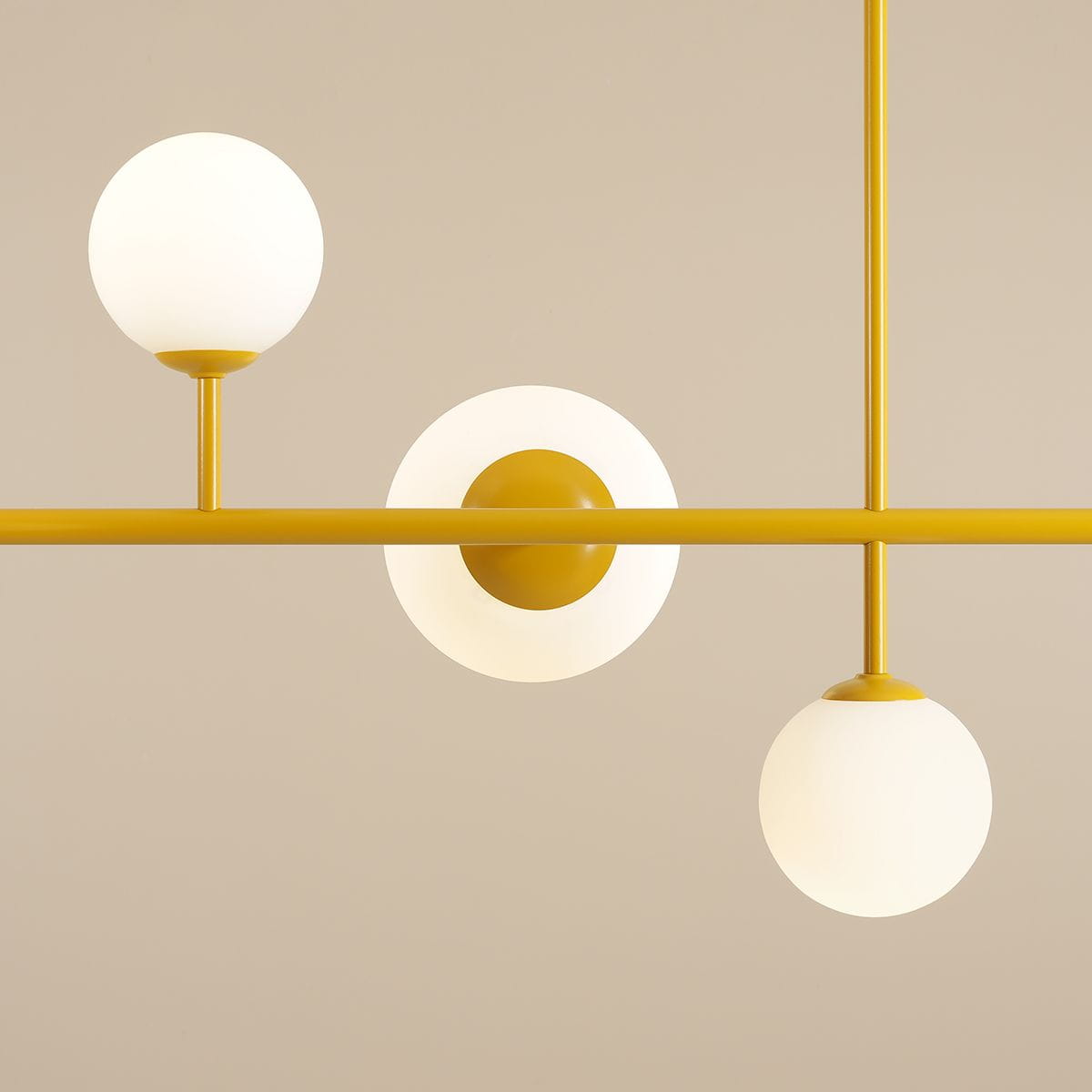 Lampa wisząca Dione 6-punktowa w kolorze żółtym, z trzema białymi, okrągłymi kloszami umieszczonymi na poziomej rurze. Ujęcie frontalne, podkreślające minimalistyczny design i kuliste formy. Tło w jasnym odcieniu.