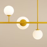 Lampa wisząca Dione 6-punktowa w kolorze żółtym, z trzema białymi, okrągłymi kloszami umieszczonymi na poziomej rurze. Ujęcie frontalne, podkreślające minimalistyczny design i kuliste formy. Tło w jasnym odcieniu.
