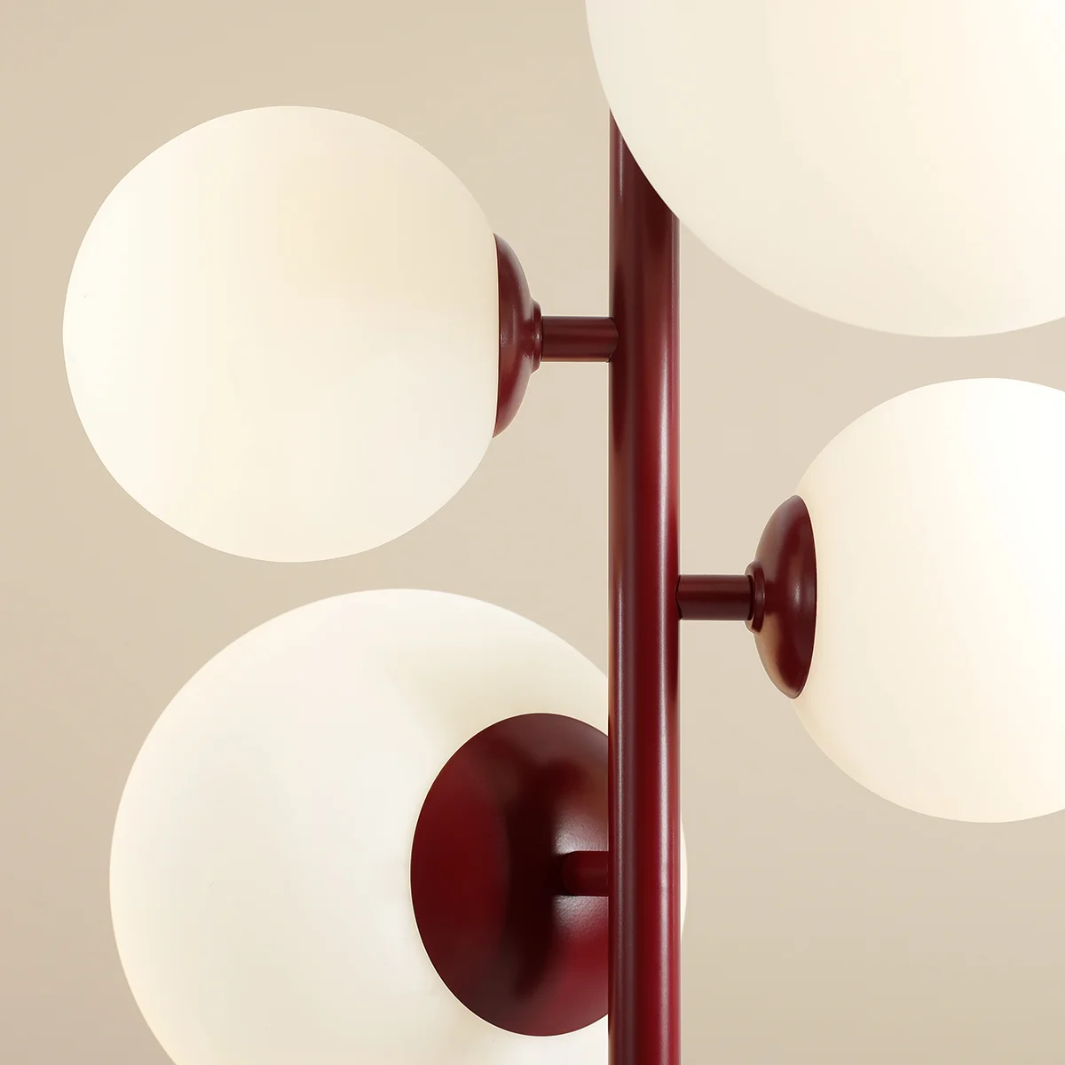 Czerwona lampa wisząca Bloom z czterema okrągłymi kloszami z mlecznego szkła. Klosze umieszczone są na metalowej konstrukcji, która ma matowe wykończenie. Ujęcie z bliska, ukazujące detale mocowania i kształt kloszy.