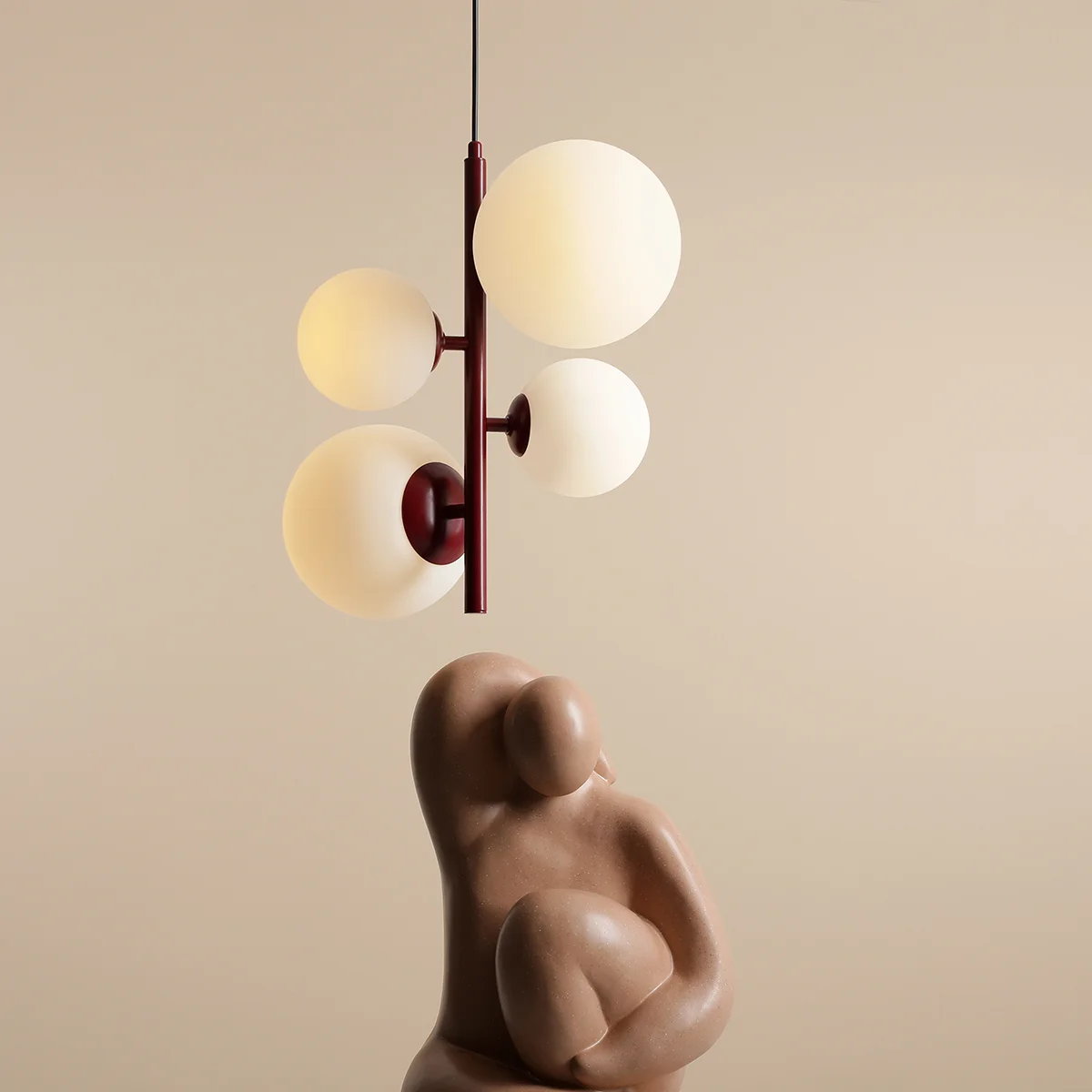 Lampa wisząca Bloom 4-punktowa w kolorze czerwonym, z metalowym stelażem i czterema okrągłymi kloszami w kolorze mlecznym. Zawieszona na cienkim przewodzie, ukazuje nowoczesny design. W tle widoczna rzeźba w kolorze beżowym.