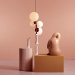 Czerwona lampa wisząca Bloom 4-punktowa z okrągłymi, mlecznymi kloszami na cienkim, ciemnym stelażu. Produkt zawieszony na długim kablu, ustawiony obok rzeźby i kolumny. Tło w odcieniu różowym, stół w jasnym kolorze.