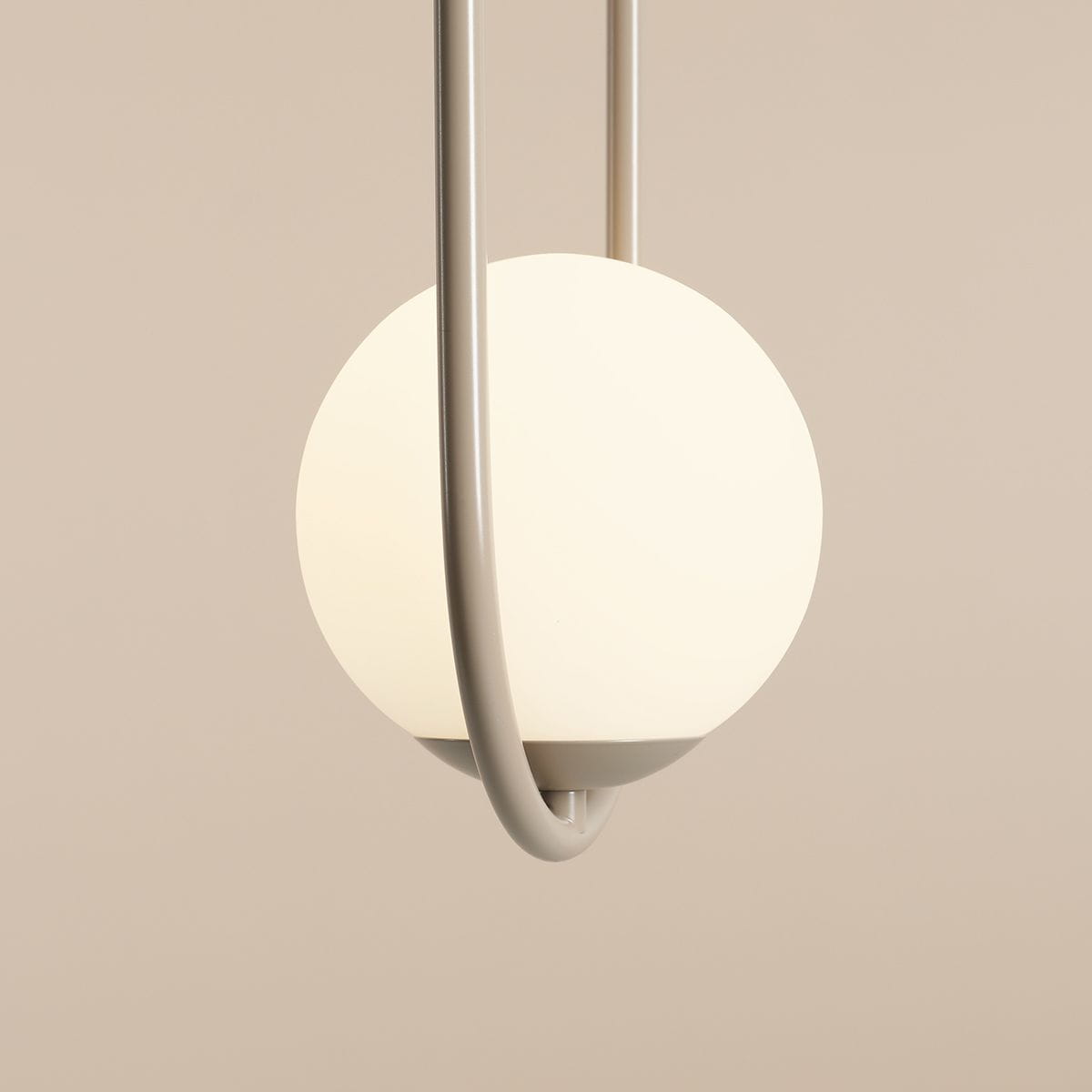 Lampa wisząca Riva 2-punktowa w kolorze beżowym, z okrągłym, mlecznym kloszem oraz metalowym mocowaniem w kształcie uformowanego łuku. Ujęcie zbliżeniowe na detal lampy, ukazujące jej elegancki design.