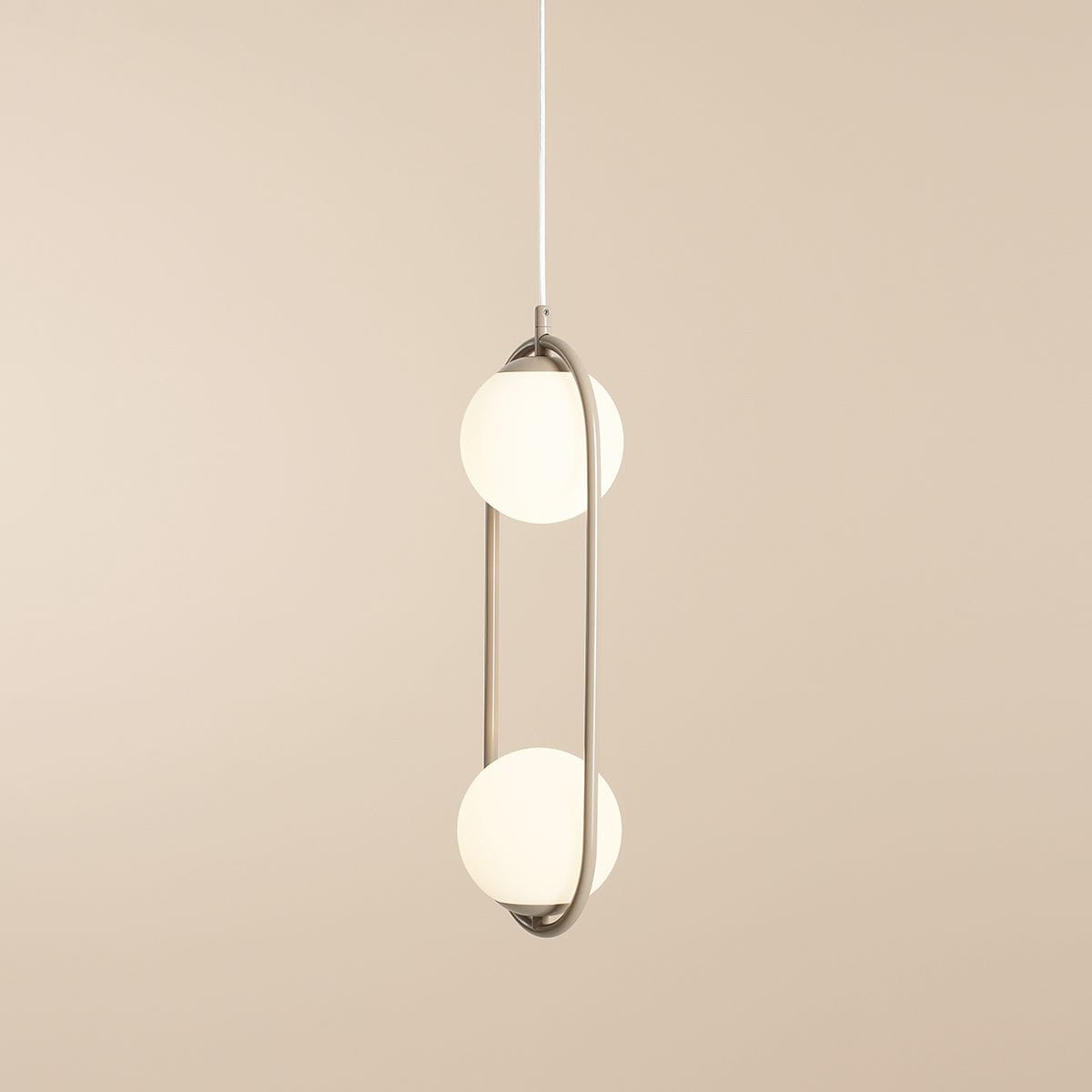 Lampa wisząca Riva 2-punktowa w kolorze beżowym, z metalowym stelażem w kształcie elipsy, zawieszona na białym przewodzie. Posiada dwa kuliste klosze z matowego szkła, emitujące miękkie światło, w prostym, nowoczesnym stylu.