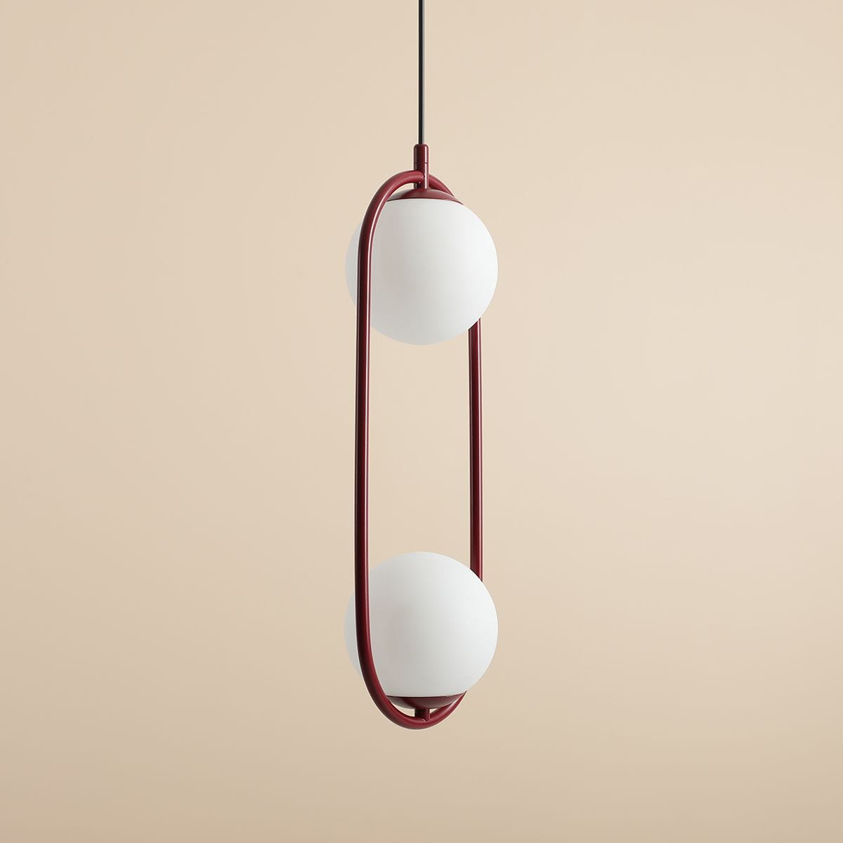 Czerwona lampa wisząca Riva 2-punktowa z białymi, okrągłymi kloszami, zawieszona na czarnym przewodzie. Kształt lampy jest geometryczny, z długim, eliptycznym ramieniem. Tło w odcieniu beżu.