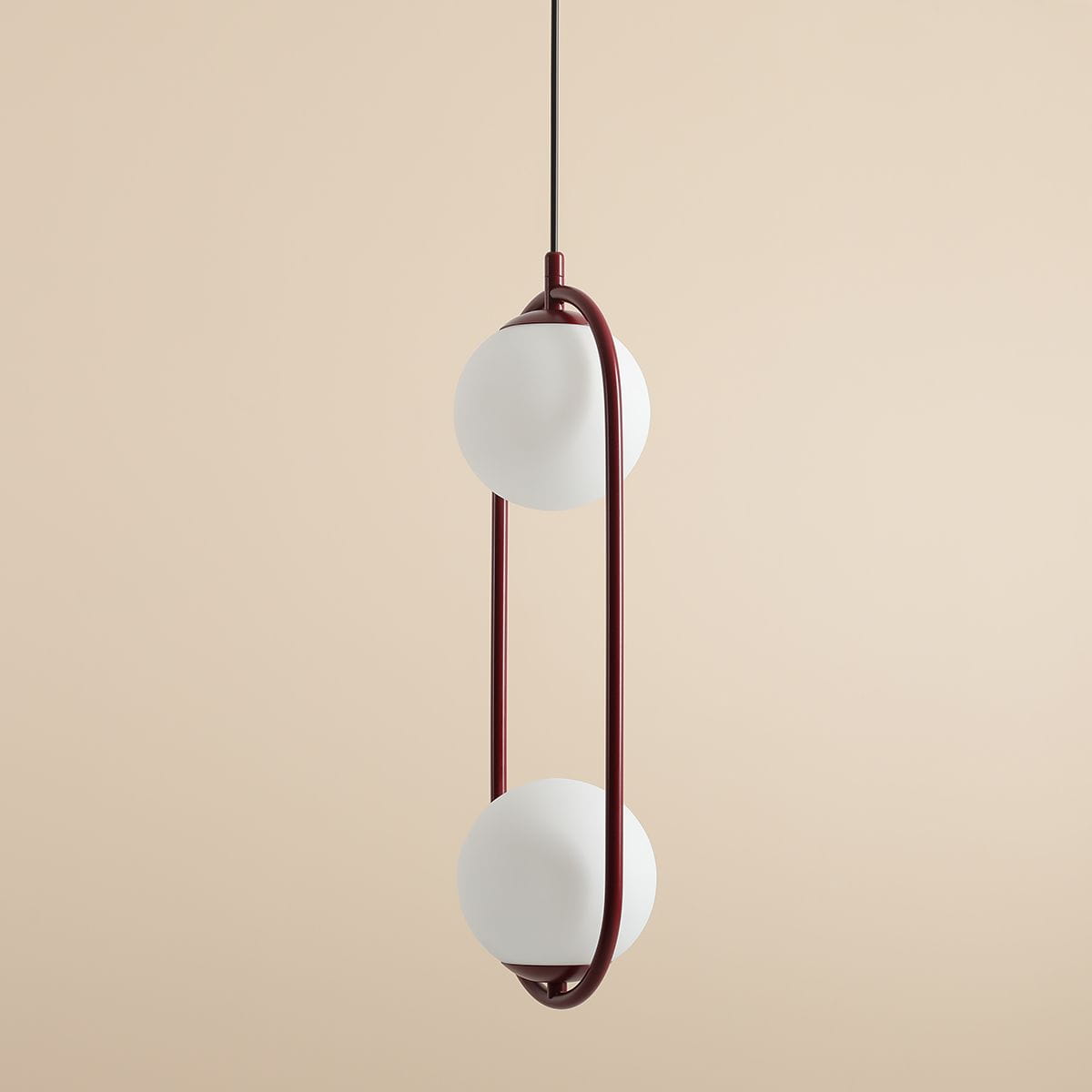 Lampa wisząca Riva 2-punktowa w kolorze czerwonym z dwiema białymi kulami, zawieszona na cienkim czarnym przewodzie. Kula znajduje się w obręczy z czerwonego metalu, tworząc nowoczesny design. Tło w odcieniu beżowym.