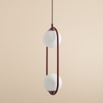 Lampa wisząca Riva 2-punktowa w kolorze czerwonym z dwiema białymi kulami, zawieszona na cienkim czarnym przewodzie. Kula znajduje się w obręczy z czerwonego metalu, tworząc nowoczesny design. Tło w odcieniu beżowym.