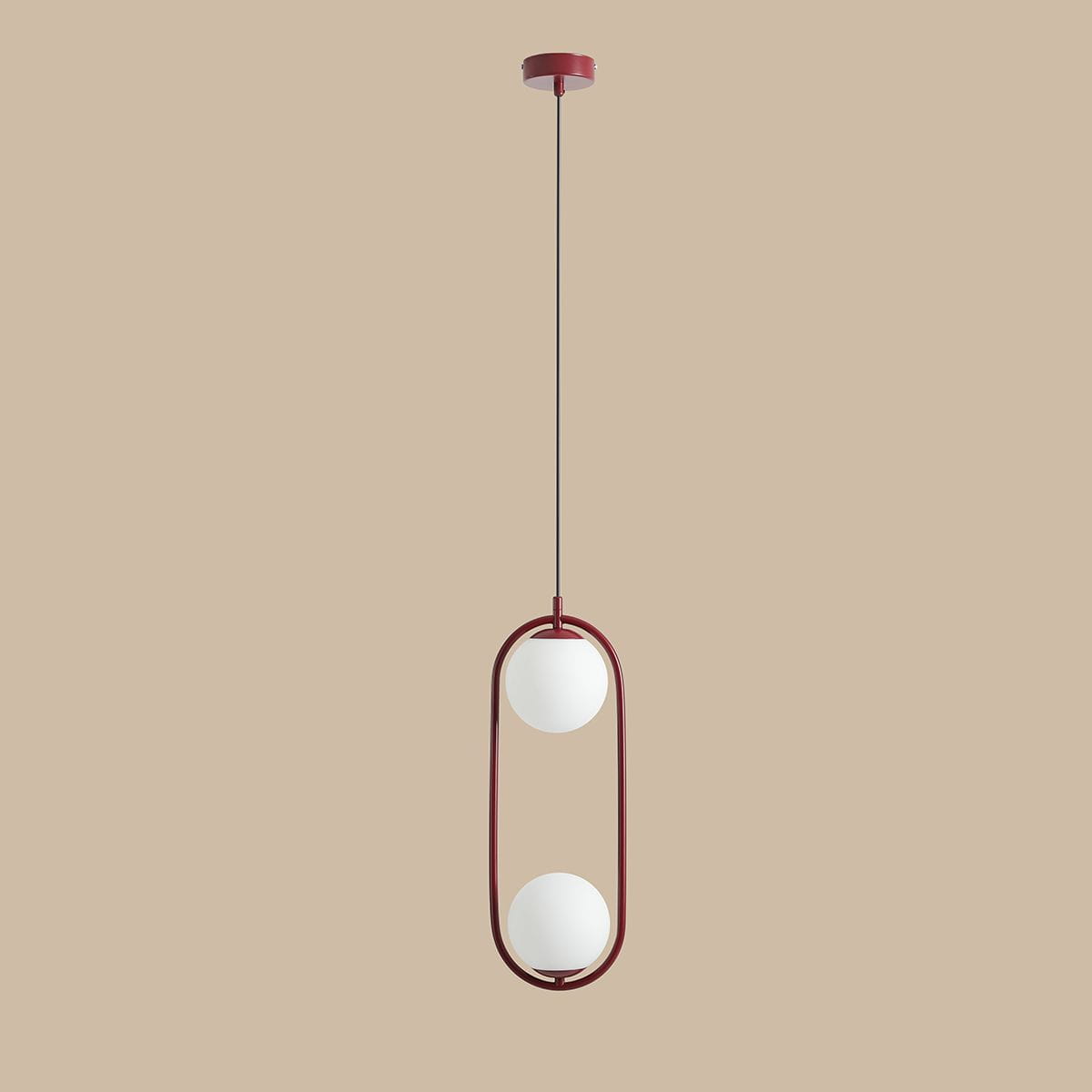 Lampa wisząca Riva w kolorze czerwonym, z dwiema białymi kulami umieszczonymi w metalowym, owalnym ramie. Produkt zawieszony na cienkim przewodzie, montowany do sufitu. Tło w odcieniu beżowym.
