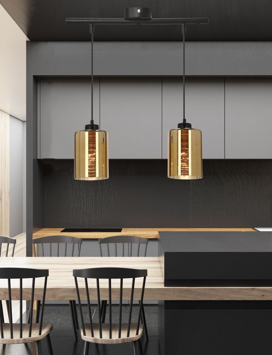 Cox lampa wisząca 2-punktowa w kolorze czarnym i złotym. Lampa zawieszona na czarnym stelażu, z dwoma cylindrycznymi kloszami w złotym, teksturowanym wykończeniu. Ujęcie z przodu, w nowoczesnej kuchni z drewnianym blatem i czarnymi krzesłami.