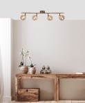 Lampa sufitowa Rodia 4-punktowa w kolorze patyny i bursztynowym, montowana na suficie. Posiada cztery okrągłe klosze, które emitują ciepłe światło, umieszczone na metalowej ramie. W tle widoczna drewniana konsola z roślinami i dekoracjami.