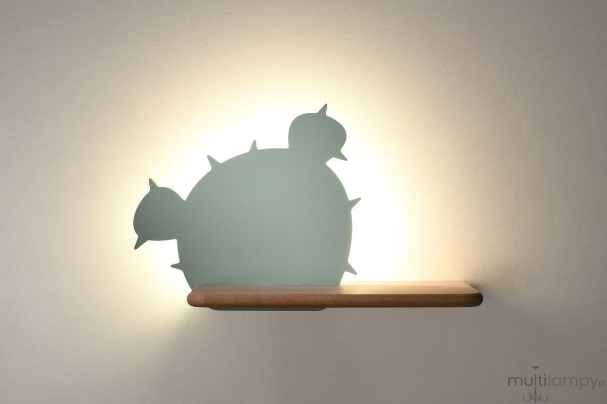 Kinkiet Cactus 3 LED w kolorze zielonym, o kształcie kaktusa, z drewnianą półką. Zdjęcie ukazuje cień rzucany przez lampę na ścianę, z efektem podświetlenia w tle. Produkt zamontowany na ścianie, z widoczną strukturą materiału.