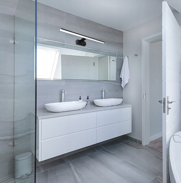 Czarny kinkiet łazienkowy LED IP44/L40/8W zamontowany nad lustrem w nowoczesnej łazience. Oświetlenie skierowane w dół, na tle szarych płytek i białej umywalki. Kinkiet ma prosty, minimalistyczny design, idealny do oświetlenia przestrzeni wokół lustra.