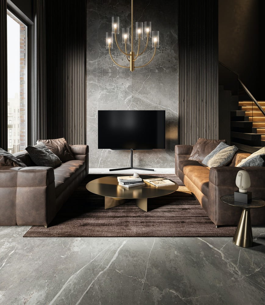 Lampa wisząca Arco 6-punktowa w mosiężnym wykończeniu z przezroczystymi kloszami. Zawieszona centralnie w nowoczesnym wnętrzu, w towarzystwie brązowych sof i okrągłego stolika kawowego. Tło z szarego kamienia dodaje elegancji.