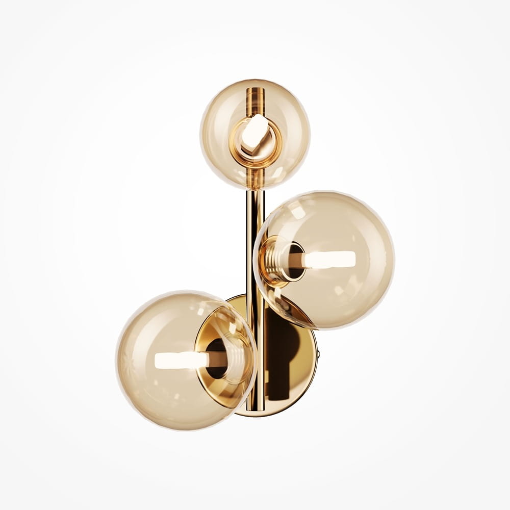 Kinkiet Dallas 3-punktowy w złotym kolorze z bursztynowymi, okrągłymi kloszami. Ułożony na ścianie, z trzema źródłami światła, metalowy stelaż z połyskiem. Tło białe, minimalistyczne, podkreślające elegancki design lampy.
