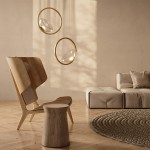 Lampa wisząca LED Lunare o mocy 5W w mosiężnej oprawie z przezroczystym kloszem, zawieszona w przestronnym wnętrzu, obok drewnianego fotela i stołka, na tle neutralnej ściany.
