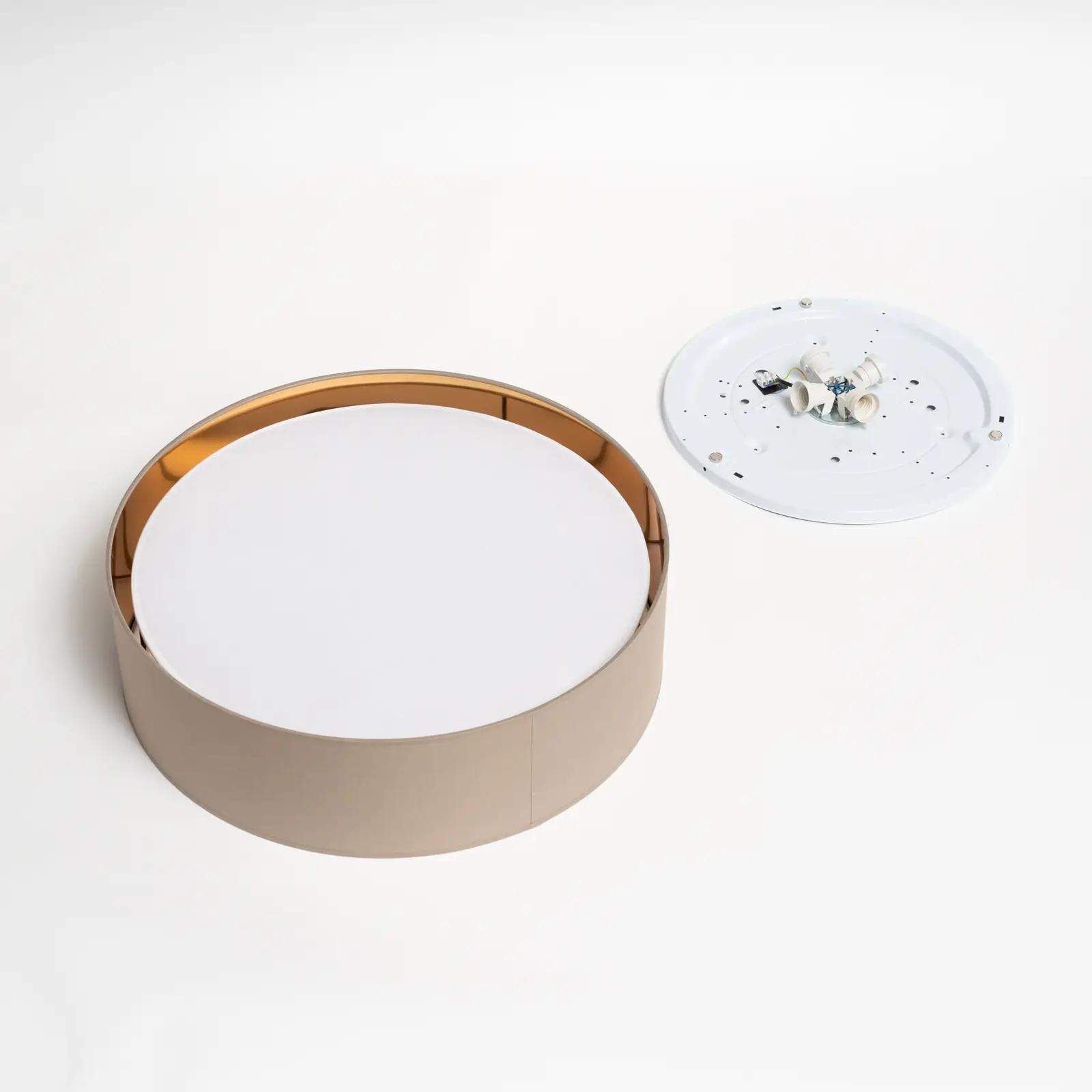 Plafon Bilbao D60 w kolorze beżowym, okrągły, z białym kloszem i złotym wykończeniem. Widać także jego podstawkę z miejscem na cztery źródła światła. Produkt leży na jasnym tle, pokazując detale konstrukcji.