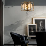 Lampa wisząca Marmo 6-punktowa w złotym wykończeniu z okrągłymi, mlecznymi kloszami. Zawieszona w eleganckim wnętrzu z marmurową ścianą. Produkt ułożony w centralnej pozycji, tworzy nowoczesną aranżację.