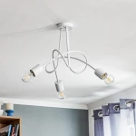 Lampa wisząca Tango 3-punktowa w kolorze białym, z trzema żarówkami na skręconych przewodach. Ujęcie z dołu, wisząca pod sufitem. W tle szare ściany oraz zasłony. Prosta konstrukcja z estetycznymi detalami.