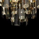 Lampa wisząca Flare 8-punktowa w kolorze złotym, z przezroczystymi, szklanymi kryształami o różnorodnych kształtach, zawieszona w pionie. Widoczny detal kryształów odbijających światło, na czarnym tle.