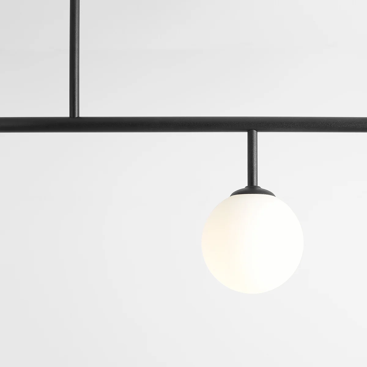 Czarna lampa sufitowa Dione 4-punktowa z metalowym stelażem i białymi, okrągłymi kloszami z matowego szkła. Ujęcie z dołu, pokazujące detale konstrukcji oraz jeden z kloszy. Tło jednolite, jasne.