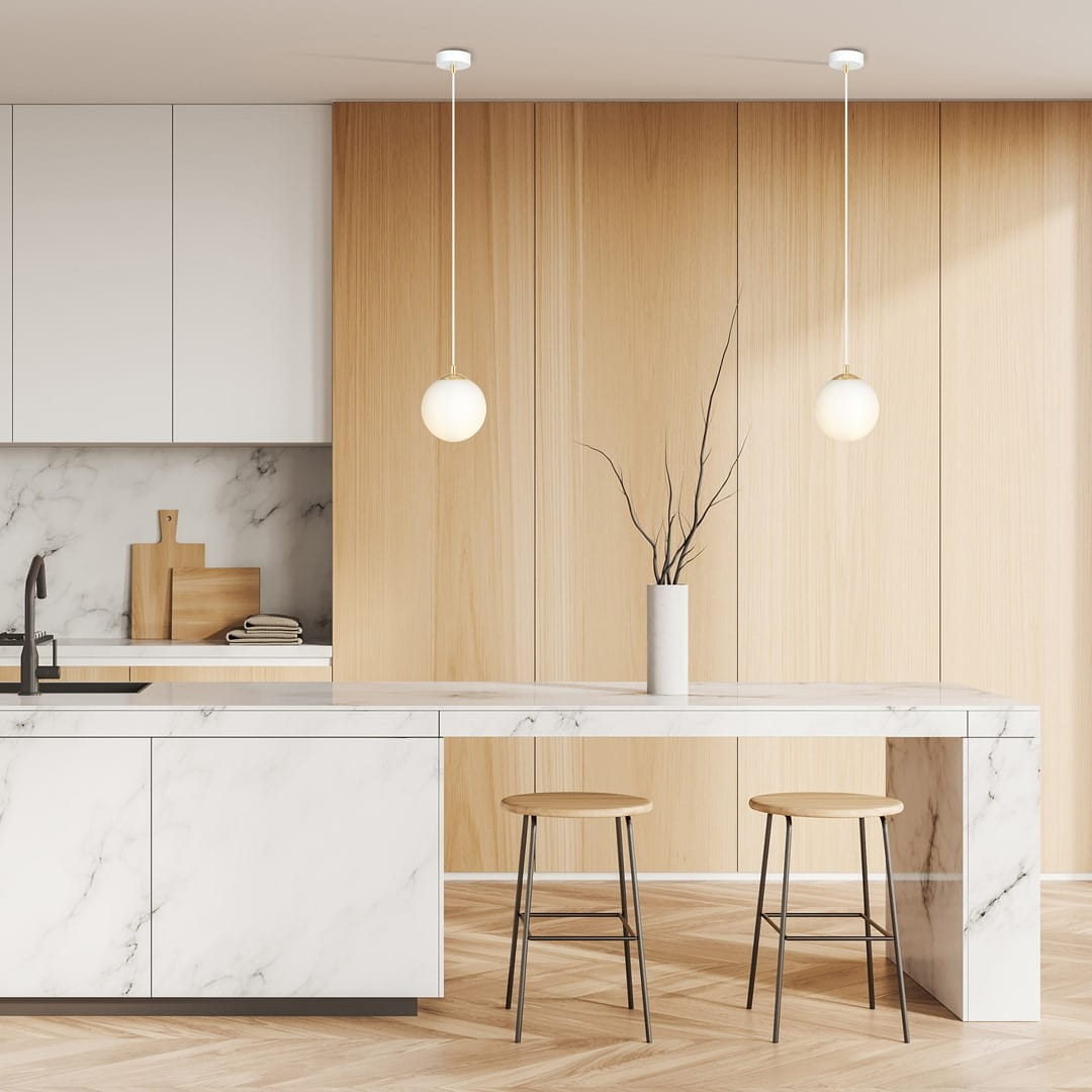 Lampa wisząca Royal 1-punktowa w kolorze białym z elementami złotymi, z okrągłą kloszem, zawieszona na cienkim przewodzie. Widoczna w nowoczesnej kuchni z marmurowym blatem i drewnianymi detalami. Tło jasne, z drewnianymi ścianami.