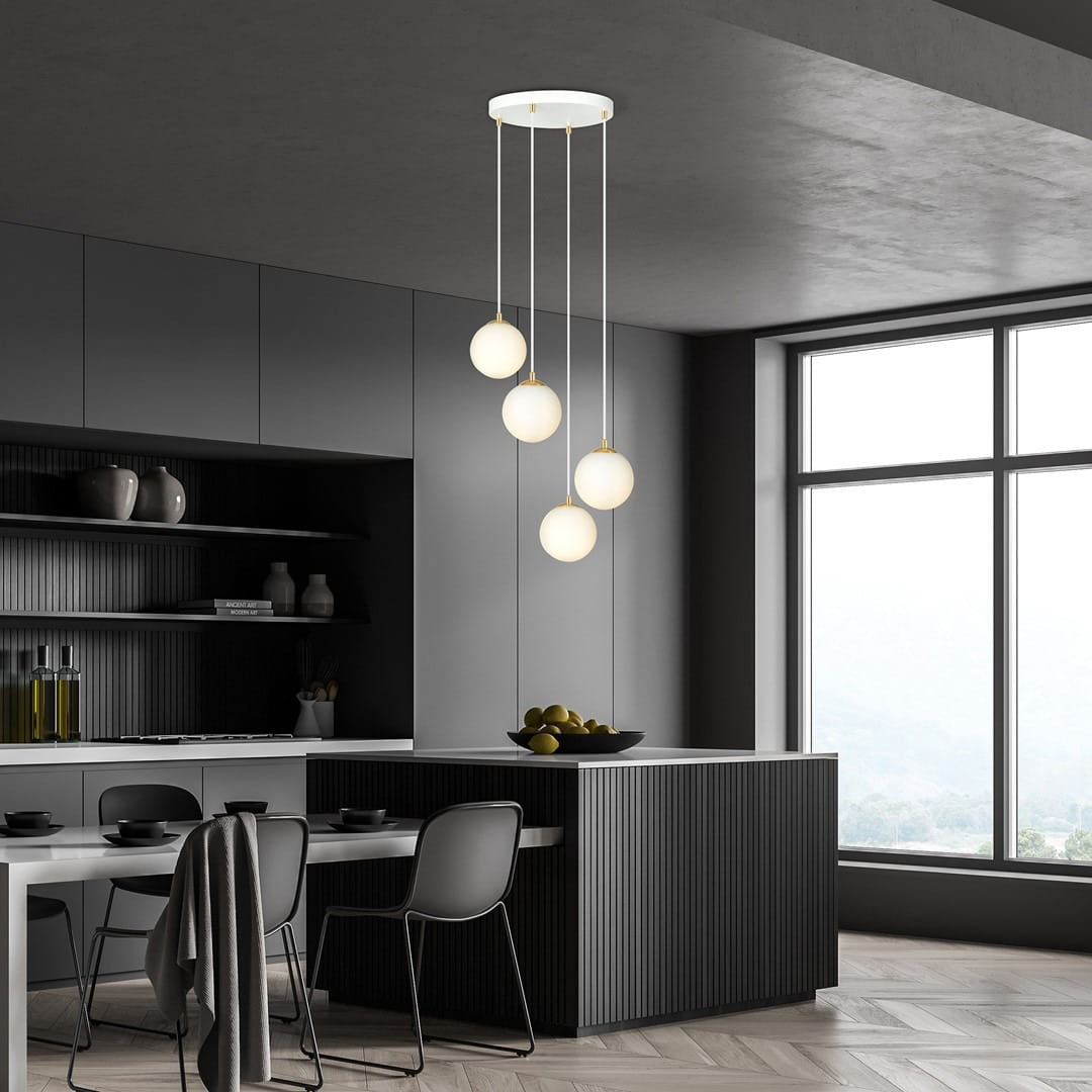 Lampa wisząca Royal 4-punktowa w kolorze białym i złotym, z czterema okrągłymi kloszami z mlecznego szkła, zawieszona na długich linkach. Ujęcie z dołu, w nowoczesnej kuchni z ciemnymi meblami i dużymi oknami.