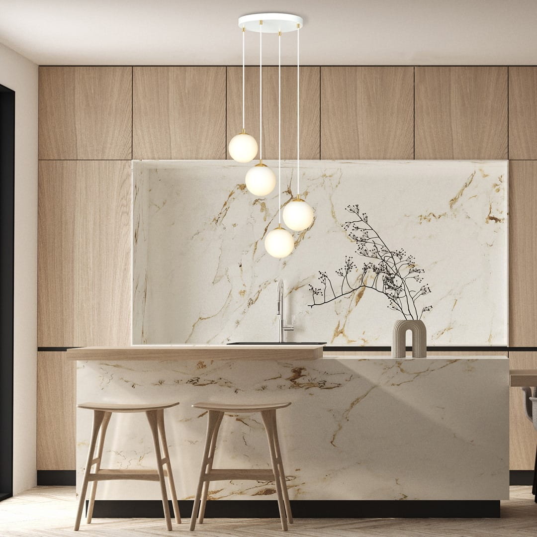 Lampa wisząca Royal 4-punktowa w białym i złotym kolorze. Zawieszona na długich linkach, z czterema okrągłymi kloszami w białym kolorze. Umieszczona w nowoczesnej kuchni z drewnianymi szafkami i marmurowym blatem.