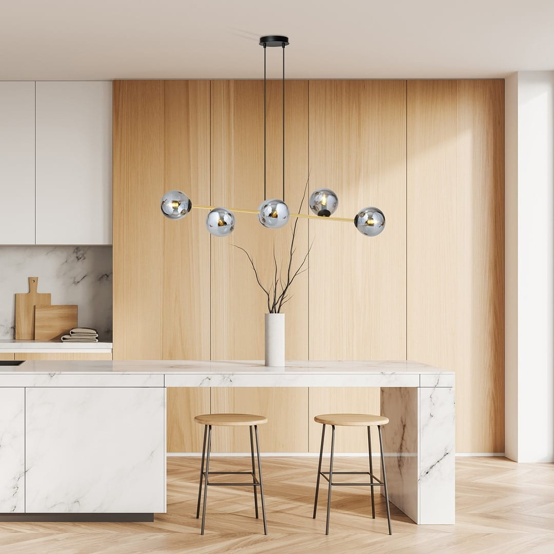 Lampa wisząca Gravity 6-punktowa w kolorze czarnym i złotym z grafitowymi akcentami, zawieszona nad białym blatem kuchennym. Posiada sześć szklanych kloszy w kształcie kul, umieszczonych na czarnym stelażu. W tle drewniane panele i minimalistyczne meble.