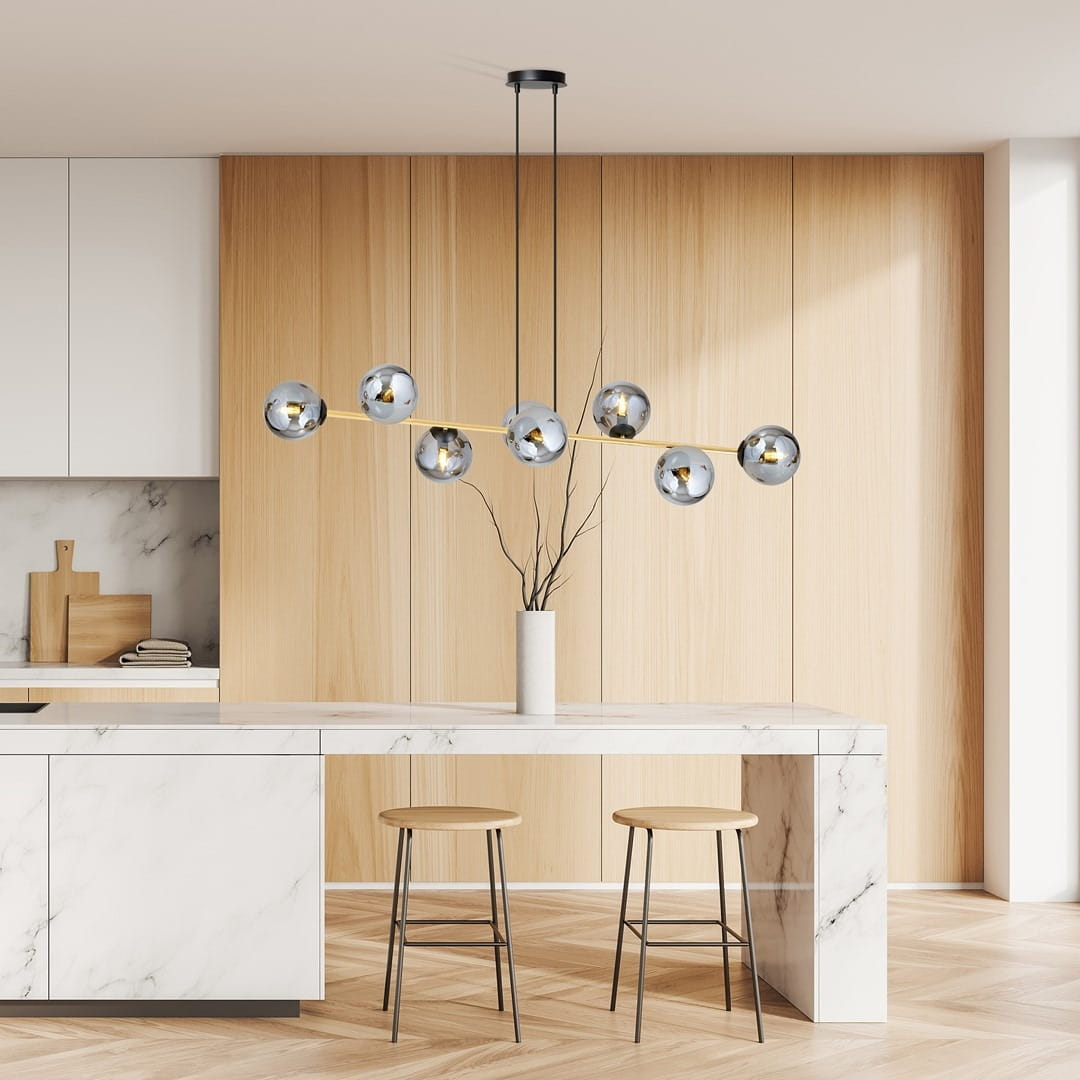 Lampa wisząca Gravity 8-punktowa w kolorze czarnym, złotym i grafitowym, z sześcioma okrągłymi kloszami, zawieszona nad białym stołem w kuchni. Klosze w kształcie kul, metaliczne, z widocznymi żarówkami. Otoczenie nowoczesne z drewnianymi detalami.
