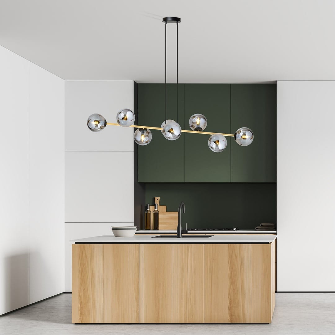 Lampa wisząca Gravity 8-punktowa w kolorze czarnym, złotym i grafitowym, z ośmioma kulistymi kloszami, zawieszona nad wyspą kuchenną. Tło w odcieniach zieleni i bieli, nowoczesne meble kuchenne z drewnianymi frontami.