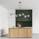 Lampa wisząca Gravity 8-punktowa w kolorze czarnym, złotym i grafitowym, z ośmioma kulistymi kloszami, zawieszona nad wyspą kuchenną. Tło w odcieniach zieleni i bieli, nowoczesne meble kuchenne z drewnianymi frontami.