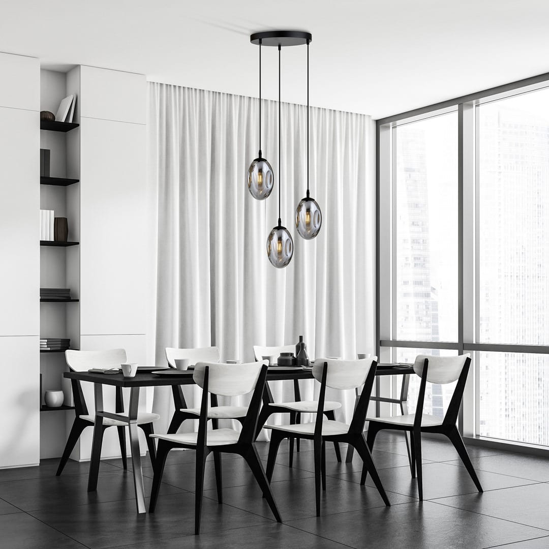 Lampa wisząca Astral 3-punktowa w kolorze czarnym i grafitowym, z trzema okrągłymi kloszami w przezroczystym szkle, zawieszona na długich linkach. Umieszczona nad stołem w nowoczesnej, minimalistycznej jadalni z białymi krzesłami i szarymi płytkami.