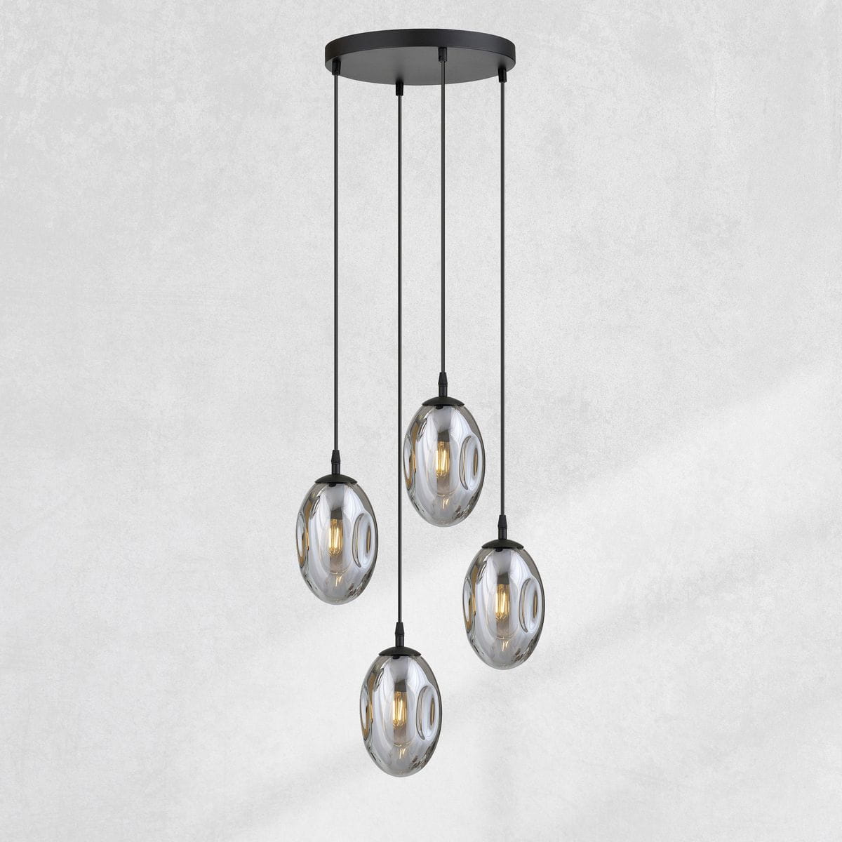 Lampa wisząca Astral 4-punktowa w kolorze czarnym i grafitowym. Cztery szklane klosze w kształcie owalu zawieszone na cienkich linkach. Metalowy sufitowy uchwyt w kolorze czarnym. Produkt zawieszony w pozycji pionowej, na jasnym tle.