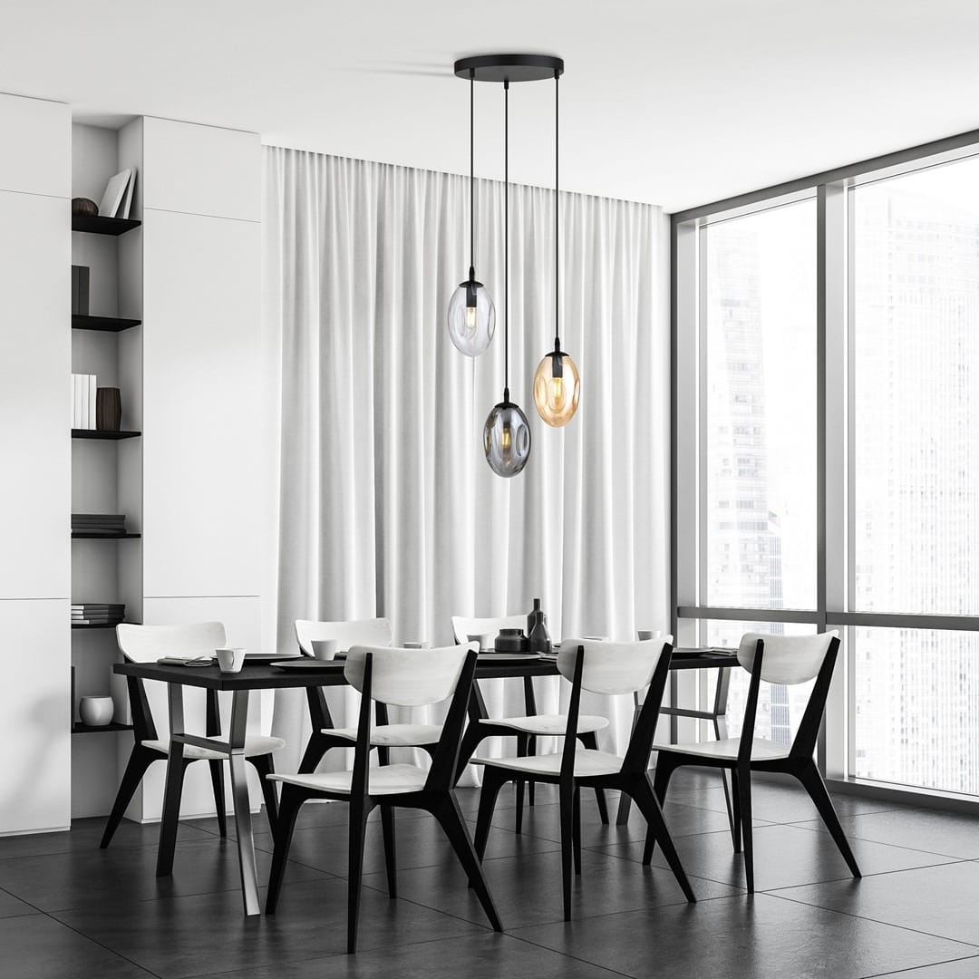 Lampa wisząca Astral 3-punktowa w kolorze czarnym z przezroczystymi kloszami w odcieniach multikolorowych. Produkt zawieszony na trzech linkach, umieszczony nad czarnym stołem w nowoczesnej jadalni z białymi krzesłami.