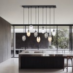 Lampa wisząca Astral 9-punktowa w czarnym kolorze z multikolorowymi kloszami w kształcie owalnym. Zawieszona na długich przewodach z metalowym mocowaniem, umieszczona nad nowoczesnym wyspą kuchenną, w jasnym wnętrzu z dużymi oknami.